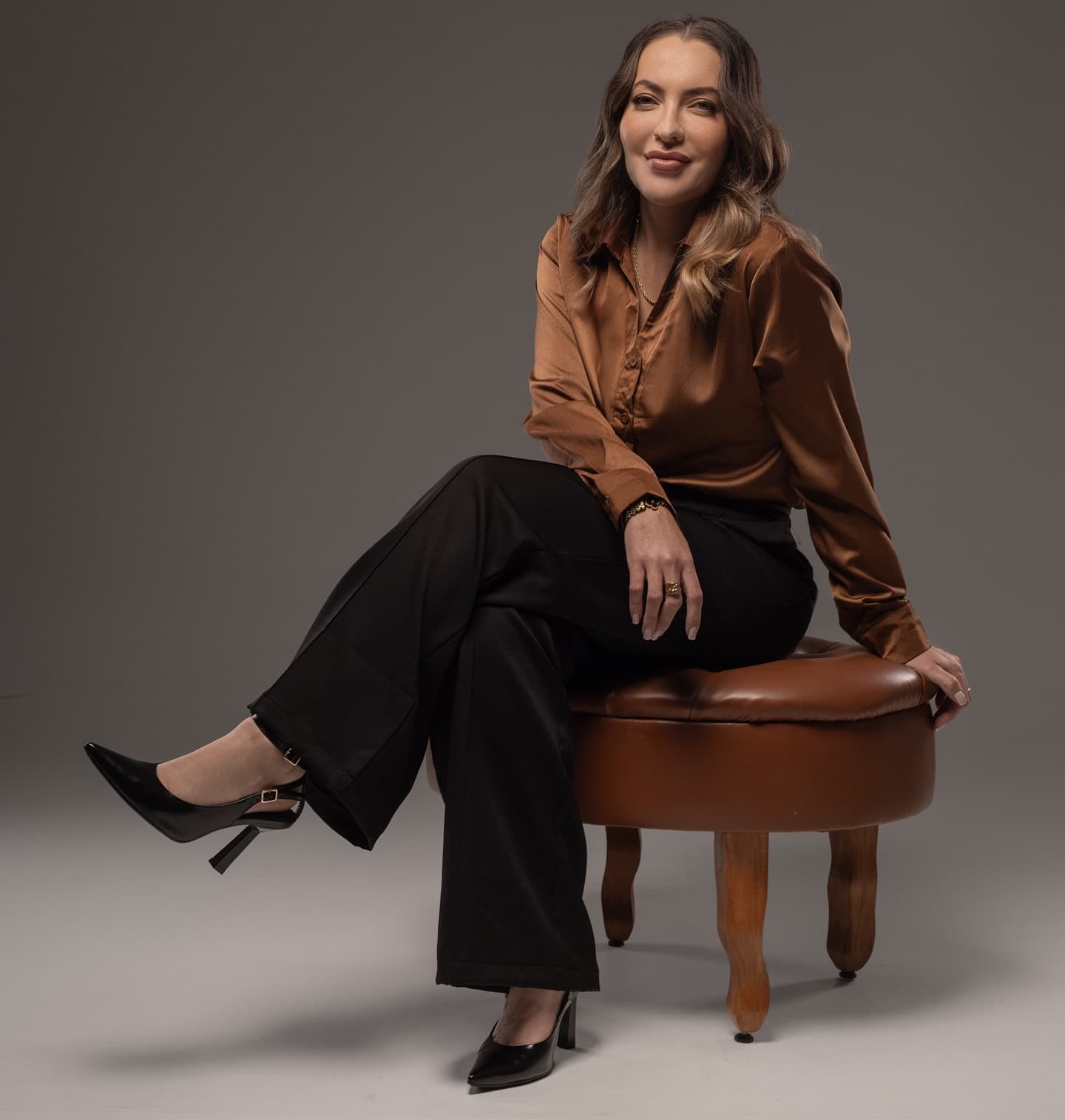 Dra. Josiane Cardoso sentada num banco de couro, de camisa caramelo e calça preta